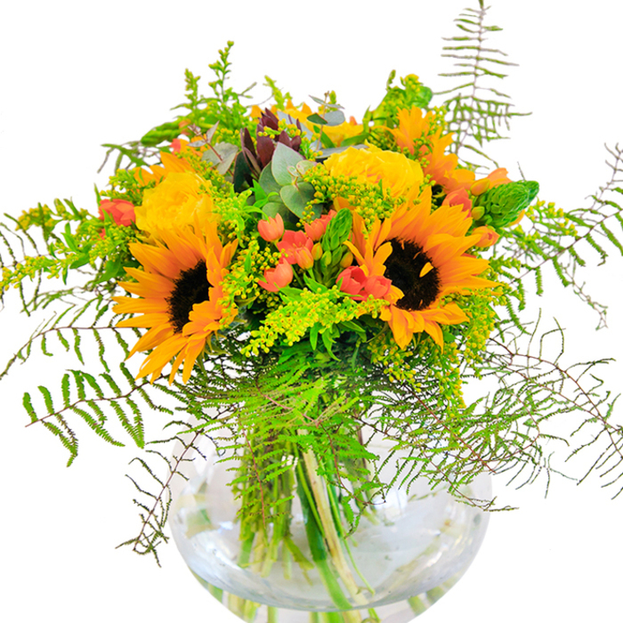 The initial impression of this Belmont-crafted bouquet is one of pure golden joy-a composition that glows with the warmth of a summer's day in the heart of the borough. Towering sunflowers and plush yellow garden roses form the main chorus, their overlapping petals layering shades of yellow, gold, and orange in a radiant symphony. Throughout the arrangement, scarlet Hypericum berries sparkle like drops of laughter, set off dramatically against lush sweeps of feathery fern fronds and airy, goldenrod-flecked greenery. The bouquet brims with texture: the velvety grain of sunflower petals, the intricate spirals of rose blooms, and crisp, fresh eucalyptus leaves that peek through to add a note of rustic wildness. Everything is anchored in a perfectly clear, rounded glass vase, whose fluid lines and water-bright clarity showcase the natural architecture of each meticulously selected stem. Lit by soft daylight, the entire display radiates a feeling of optimism and celebration-an ideal centerpiece for local festivities or intimate gatherings. As Belmont Flowers, we pride ourselves on capturing the area's welcoming charm; this bouquet is the embodiment of that spirit, made for memorable moments like birthdays, anniversaries, or simply to bring the glowing spirit of Belmont into any home.