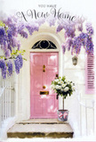 This photograph shows a tranquil, romantic doorway that feels as though it belongs on a peaceful Belmont lane, where neighbours pause to admire each other's flowers. A pale pink front door, subtly weathered in places, stands at the centre of the image, glowing softly against crisp white walls. Above it, long tendrils of wisteria spill down from an unseen trellis, their lavender and lilac blooms gathering in loose, abundant clusters that form a dreamy floral curtain. The wisteria's feathery leaves interrupt the blooms with flecks of green, casting gentle patterns of shadow across the paintwork and stone. Just in front of the door, placed thoughtfully on the doorstep, a metal florist's bucket brims with freshly cut white and cream roses. Their heads are full and rounded, petals layered tightly at the centre and loosening at the edges, catching the light in subtle ivory and butter tones. Sprays of greenery thread between the roses, offering a natural contrast in texture and colour, like a small, carefully curated garden brought right up to the threshold. Around the bucket, a slim pink ribbon is tied into a neat bow, its satin sheen catching glints of light and echoing the door's pastel hue. The overall lighting feels like late afternoon, perhaps after a same-day delivery from a local Belmont florist, with a calm glow that wraps the whole scene in warmth. Everything about this composition speaks of welcome and gentle hope, ideal for marking a housewarming, a new chapter, or simply to make a familiar Belmont doorway feel newly cherished.